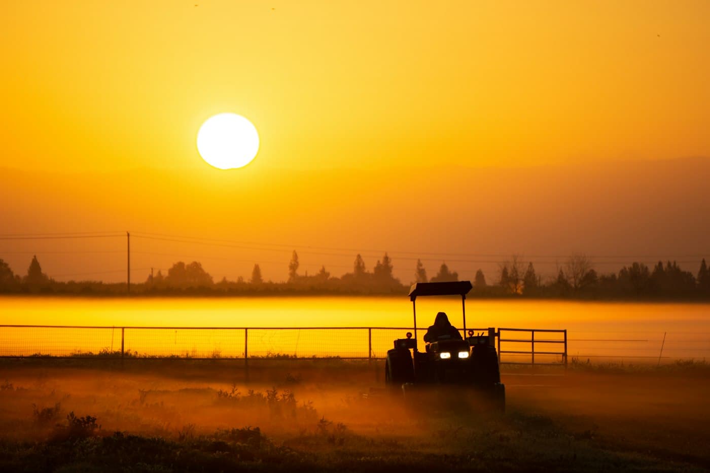 Trator trabalhando em um campo ao nascer do sol, com neblina