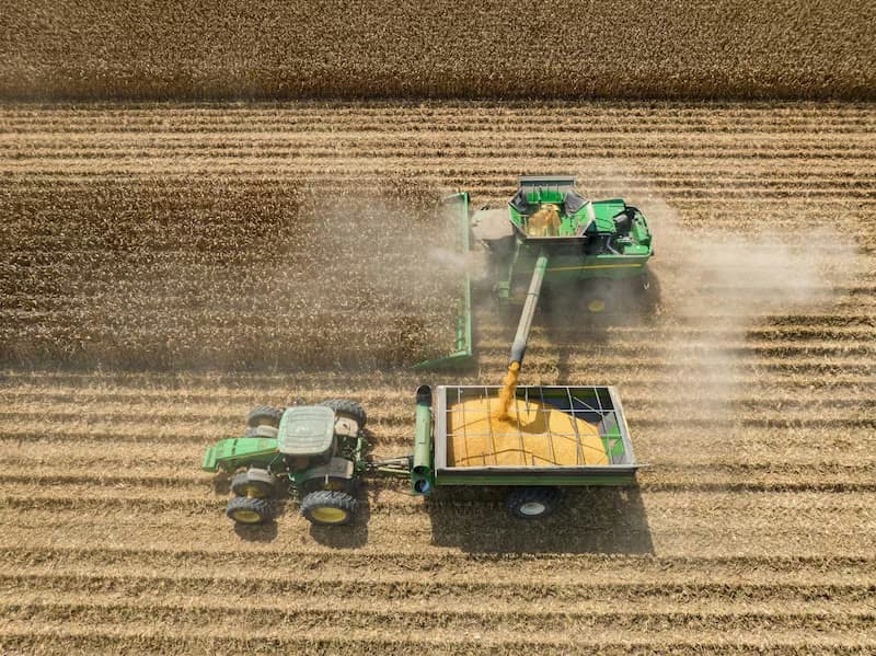 Aerial view of a combine unloading corn into a tractor-drawn grain cart
