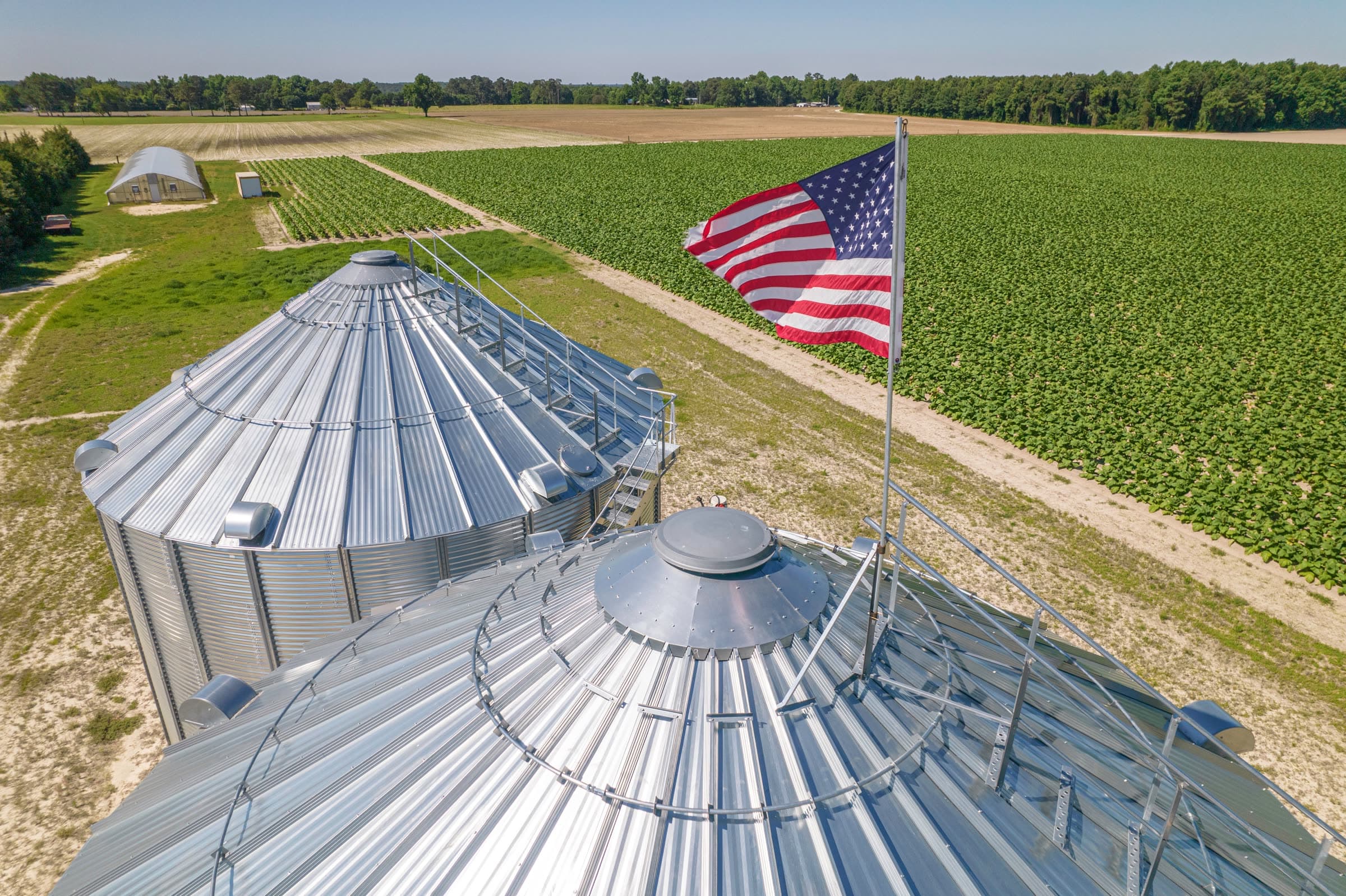 United States flag flying over grain silos on a farm, with crop fields behind